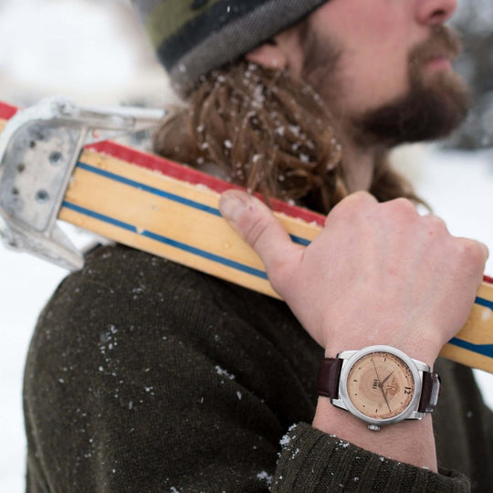 Man in winter gear wearing a handcrafted wood watch holding a vintage ski, showcasing style and outdoor spirit.